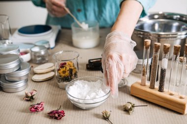 Koruyucu eldiven takan eller, eczacı malzemeleriyle çevrili cam kavanoza beyaz toz doldurur. Yavaş güzellik ritüeli, dikkatli cilt bakımı, sakinleştirici DIY süreci, duyusal formülasyon