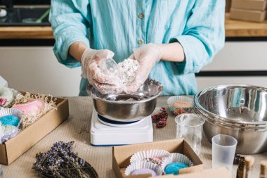 Eller, hediye kutularıyla çevrili metal kasenin üzerinde büyük beyaz bir banyo bombası tutuyor. Sanatsal formülasyon, kusursuz el yapımı, kozmetik aletler, profesyonel üretici