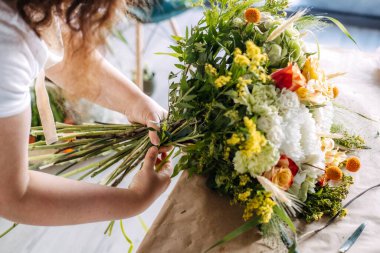 Çiçekçi çiçek buketini ahşap çalışma alanının üzerinde kurdele ve çiçek saplarıyla tamamladı. Çiçek tasarım ana sınıfı, deneyimli perakende satış, elle çalışma..