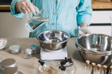 Dijital ölçekte insan cam sürahiden metal kaseye sıvı döker. Kozmetik emülsiyon fiziği, yağ ve suyu karıştırma estetik, cilt bakımı bilimi, profesyonel krem üretimi