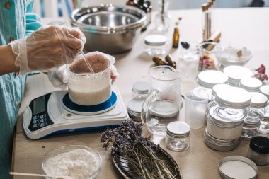 Eldivendeki eller dijital ölçekte beyaz sıvıyı karıştırmak için cam çubuk kullanır. Ürün dönüşümü, çiğ-hazır, sanatsal cilt yolculuğu, markanın arkasında.