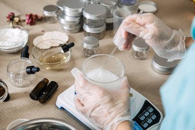 Dijital ölçekte cam şişede beyaz sıvıyı karıştırmak için cam çubuk kullanıyor. Moleküler cilt bakımı, aktif bileşen çözücü, fonksiyonel güzellik zanaatı, hassas kozmetik ölçüm