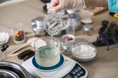 Eldiven giyen biri dijital ölçekte cam kavanoza temiz sıvı döker. Mikro küme güzellik, küçük işletme üretimi, el yapımı nemlendirici, el yapımı güzellik laboratuarı.