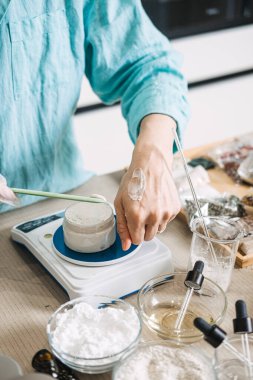 Eldivenli kişi, kavanozu dijital ölçekte ölçerken spatulayla elden ele krem sürer. Dermatolojik testler, bitkisel losyonlar, organik ürün tasarımı, ekolojik bilinçli güzellik