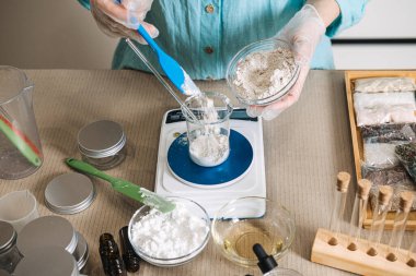 Dijital ölçekte yerleştirilmiş küçük cam kase barutunu tutan eller. ham güzellik malzemeleri, cilt şeffaflığı, minimalist formülasyon, doğal kozmetik bileşenler