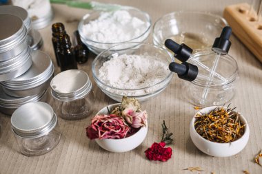 Kurumuş çiçek yaprakları ve tozlar seramik kaselerde cam pipetler ve metal tenekelerin yanında dururlar. tam bitkisel cilt bakımı, botanik yağ karışımı, çiğ çiçek yaprağı boyası, güneş yağı.