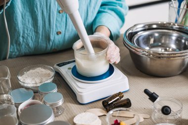 Dijital ölçekte cam kavanoza sıvı bazlı karıştırmak için daldırıcı kullanan kişi. Kozmetik öykünme, profesyonel krem karıştırma, cilt bakımı laboratuvar aletleri, losyon yapma süreci