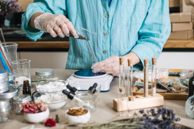 Hands in gloves pour dark botanical dusts from packet into glass test tube on digital scale. Botanical dusts, adaptogenic powders, fresh mixing, mineral boosters