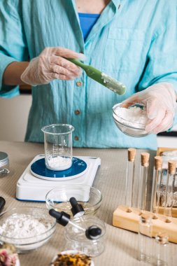 Kişi, dijital ölçekte beyaz tozu cam şişeye aktarmak için yeşil spatula kullanır. Temiz güzellik bilimi, çevre dostu laboratuvar, doğal formül uzmanı, sürdürülebilir güzellik zanaatı.