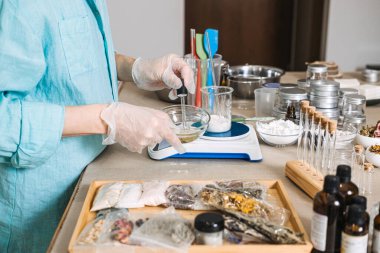 Person in gloves uses glass pipette to dispense liquid into beaker with white powder on digital scale. cosmetic chemistry aesthetic, lab-style skincare diy, precise formulation, apothecary workshop