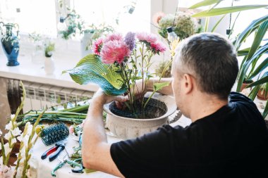 Evde dikkatli bir çiçek aranjmanı yapan bir adam. Çiçek meditasyon pratiği, yavaş düzenleme çiçekleri, düşünceli çiçekçilik, zen çiçeği terapisi, meditasyon çiçekleri tasarımı