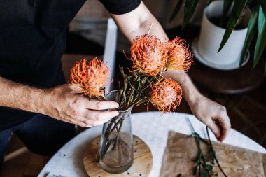 Kişi portakal iğnelik protezini cam vazoya yerleştirir. Sürdürülebilir düğünler, çevre dostu etkinlikler, geri dönüşümlü dekor, düşük etkili çiçekçilik.