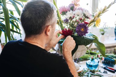 İnsanoğlunun taştan vazoda paskalya çiçeklerini dikkatlice düzenlediği arka manzara. Erkek akıl sağlığı, yaratıcı terapi, dikkatli işçilik, duygusal düzenleme, erkekler için stres atma, klişeleri kırma..