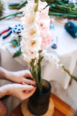 Adamın elleri çiçek aranjmanı sırasında açık renkli gladiolusu vazoya yerleştirir. Terapi amaçlı bahçıvanlık, yaratıcı kaçışçılık, işçilik yoluyla stres atma, düşünceli hobiler.