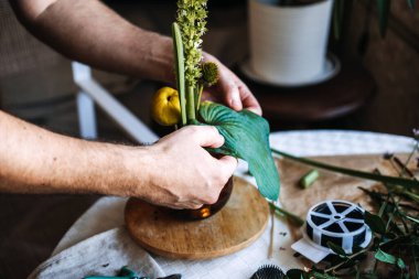 Eller ahşap tabanda kehribar cam vazoda büyük yeşil yaprak ve botanik elementler düzenler. Sanat terapisi, çiçek meditasyonu, stres atma aktiviteleri, farkındalık pratiği, dokunsal nişan