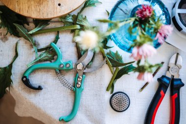 Çiçekçi çalışma alanının en üst görüntüsünde çiçek kurbağası ve çiçek saplarının yanında budama makası ve tel kesiciler bulunur. Çiçek atölyesi, küçük işletme girişimcisi, yaratıcı çalışma alanı, çiçekçilik ana sınıfı..