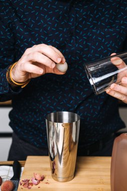 Barmen, liçi meyve kabuğu ve camın yanına paslanmaz çelik kokteyl karıştırıcısına döker. El yapımı kokteyl hareketi, profesyonel barmen, miksoloji teknikleri, lichee martini, zanaatkar içkileri.