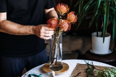 Kişi portakal iğnelik protezini cam vazoya yerleştirir. Sürdürülebilir düğünler, çevre dostu etkinlikler, geri dönüşümlü dekor, düşük etkili çiçekçilik.