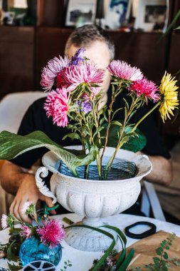 Adam süslü beyaz kaide vazosunda parlak paskalya çiçekleri düzenliyor. Sürdürülebilir mekanikler, yeşil yaşam, bahçeden vazoya, çevreye duyarlı hobi