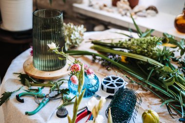 Yukarıdan bakıldığında çiçekçi aletleri ve çiçek düzenleme için botanik saplarıyla çevrili akıllı telefon görünüyor. Çiçekçilik, botanik eğitimi, yaratıcı çiçek düzenleme kursu.