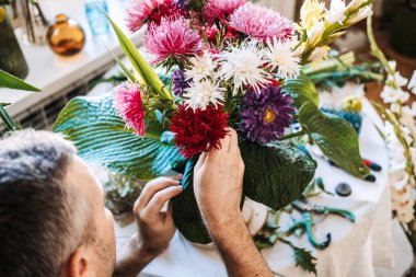 Adam paskalya çiçekleri ve büyük yeşil yaprakları klasik vazoda düzenler. Erkekler için stres yönetimi, tedavisel çiçekçilik, kortizol azaltma, dikkatli işçilik, erkek sağlığı