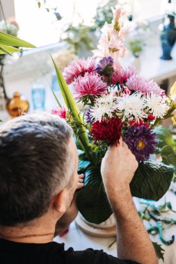 Adam paskalya çiçekleri ve büyük yeşil yaprakları klasik vazoda düzenler. Erkekler için stres yönetimi, tedavisel çiçekçilik, kortizol azaltma, dikkatli işçilik, erkek sağlığı