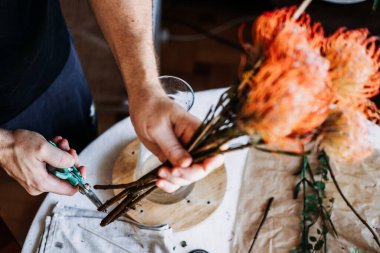 Elleri cam vazoya yerleştirmeden önce turuncu iğnelik protezin gövdesini budarlar. Zanaatkar çiçekçiler, lüks ev aksanları, üst düzey çiçekçiler, eşsiz iç mimari..