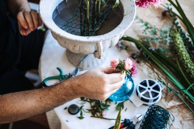 Erkek ellerinin, çiçek aletleri ve beyaz metal vazo ile pembe paskalya çiçeğini masanın üzerinde tutması. Yavaş çiçek hareketi, yerel çiçek çiftliği, mevsimlik çiçekler, yerli çiçek endüstrisi.