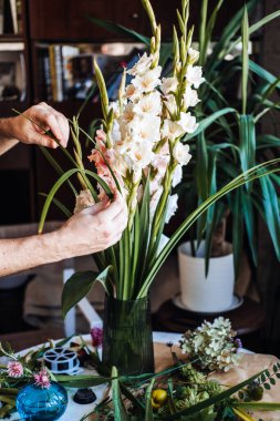 Adam uzun gladiolus çiçeklerinin etrafında siyah cam vazoda yeşil yaprakları şekillendiriyor. Yaratıcı meditasyon, düşünceli hobiler, stres için çiçek düzenleme, zihinsel sağlık sanatı, yavaş yaşam