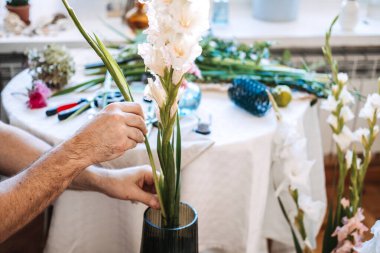 İnsanın elleri dikkatlice uzun gladiolus 'u flütlü cam vazoya yerleştirir. Ruh sağlığı, DIY çiçek atölyesi, botanik terapisi.