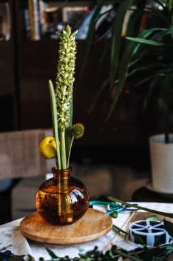 Eller, ahşap zemindeki kehribar cam vazodaki botanik elementleri düzenler. Botanik sanat terapisi, elle tedavi, zanaat yoluyla kaygı azaltma.