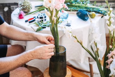 Adam Gladiolus 'u cam vazoya koyar. Mevsimlik çiçekler, yerel olarak yetişen çiçekler, gladyatör düzenlemesi, bilinçli tüketim, yavaş çiçek hareketi