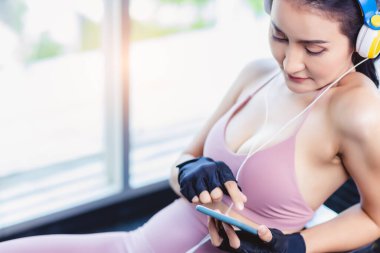 Spor salonunda spor yaparken akıllı telefon kullanan ve müzik dinlemek için kulaklık takan mutlu bir kadın. Güzel bir kız spor eldivenleri giyer. Güzel bir vücudu ve seksi bir vücudu vardır.