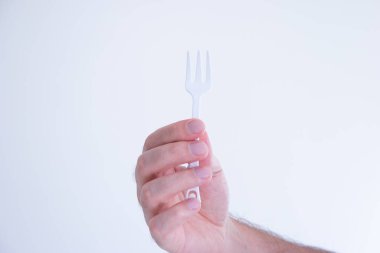 Beyaz plastik tek kullanımlık çatal beyaz tenli erkek eli tarafından tasarlandı..