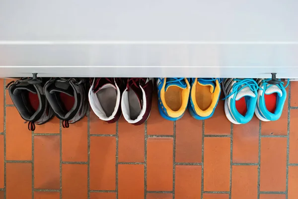 Row of used shoes lined up partially under shoe cabinet inside apartment top view.
