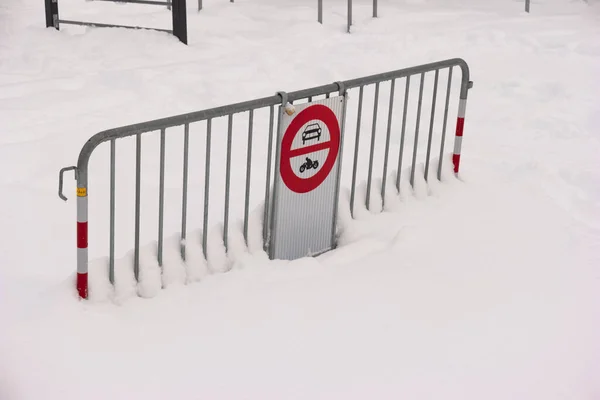 Metal road fence barrier and stop sign on snow covered entrance road to a park.