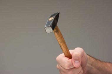 Beyaz erkek eli, gri arka planda izole edilmiş kullanılmış bir çekiç tutuyor..