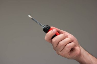 Beyaz erkek eli, gri arka planda izole edilmiş kırmızı plastik bir tornavida tutuyor..