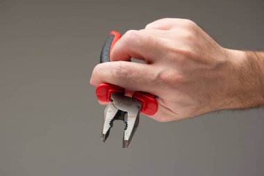 Beyaz erkek eli gri arka planda izole edilmiş kırmızı plastik saplı metal bir kerpeten tutuyor..