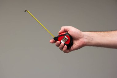 Beyaz erkek eli, gri arka planda izole edilmiş bir mezura cetveli tutuyor..