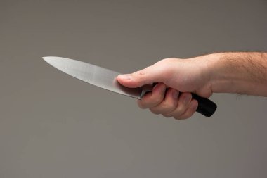 Beyaz erkek eli gri arka planda izole edilmiş büyük bir mutfak bıçağı tutuyor..
