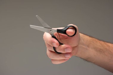 Beyaz erkek eli, gri arka planda izole edilmiş siyah plastik saplı küçük bir gemi makası tutuyor..