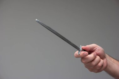 Beyaz erkek eli, gri arka planda izole edilmiş çelik bıçak keskinleştirme çubuğu tutuyor..