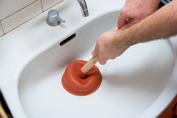 Caucasian male hand holding a plunger unclogging a bathroom sink.