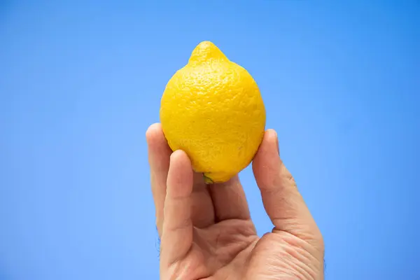 白种人男性的手拿着鲜黄色的全柠檬 蓝色背景隔离 — 图库照片