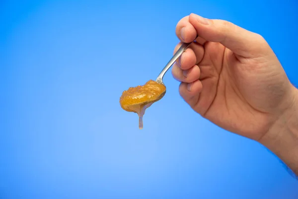 Beyaz erkek stüdyosunun elinde tuttuğu çay kaşığından taşan kristalize bal mavi arka planda izole edilmiş..