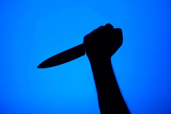Knife stabbing gesture silhouette black on blue background studio shot unrecognizable .