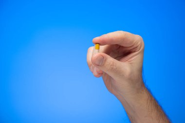 Beyaz kapsül hapları, beyaz kapsül hapları, beyaz beyaz erkek eli tarafından parmaklarının arasında tutuluyor. Mavi arka plan stüdyo çekimlerinde izole ediliyor.