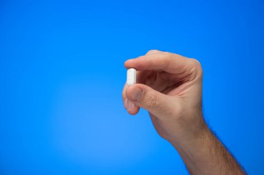 Kafkas erkek eli tarafından parmaklarının arasında tutulan beyaz ilaç mavi arka plan stüdyo çekiminde izole edildi.