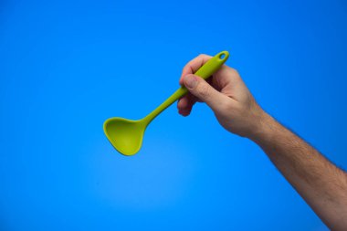 Beyaz erkek elinde silikon servis kepçesi mavi arka planda izole edilmiş..